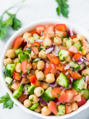 vegan chickpea salad in a white bowl with fresh parsley scattered on table