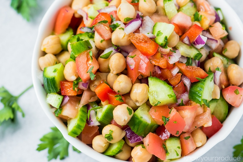 chickpea salad with fresh vegetables in a white bowl on marble slab with parsley scattered