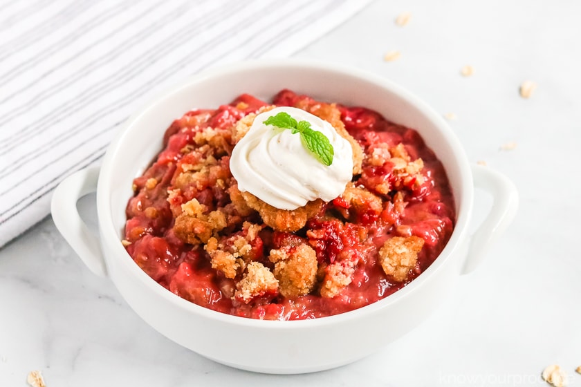 strawberry rhubarb crisp in a bowl topped with coconut whipped cream