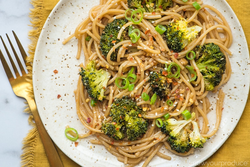 broccoli with asian noodles on a plate with mustard napkin and gold fork