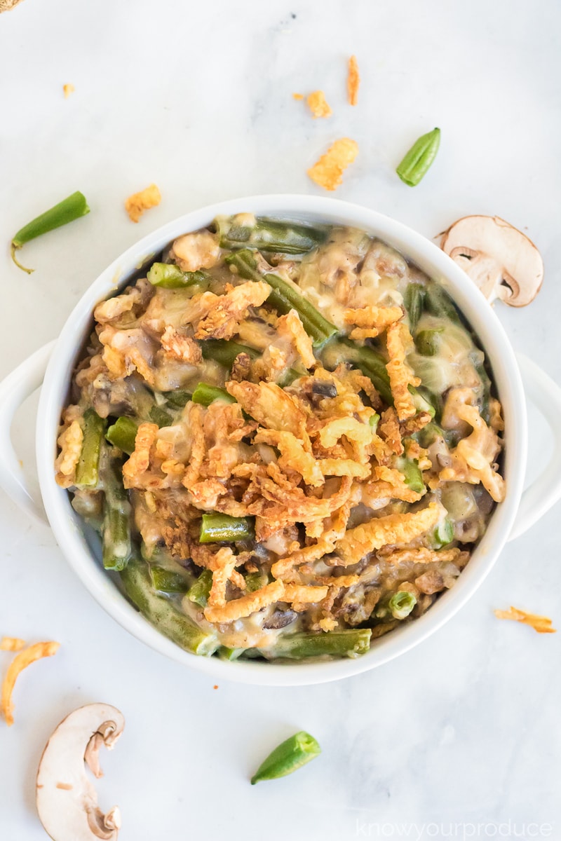vegan green bean casserole in mini cassoulet dish with sliced mushrooms, fried onions, and string bean ends scattered on marble slab