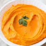 mashed carrots in a white bowl with parsley leaf as garnish