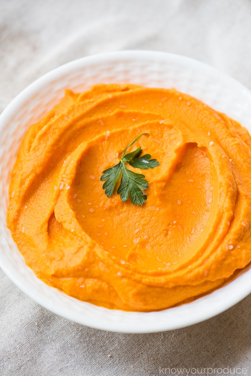 mashed carrots in a white bowl with parsley leaf as garnish