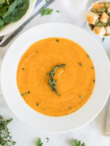 vegan butternut squash soup in a white bowl with thyme garnish