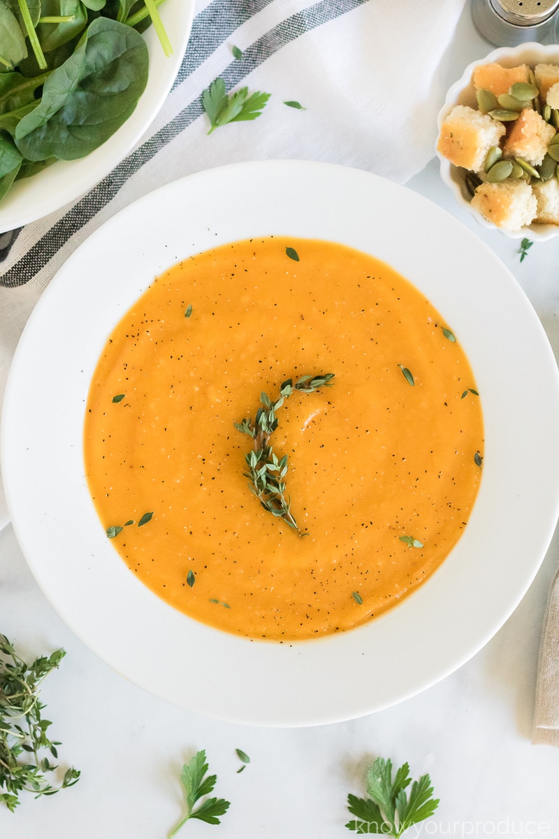vegan butternut squash soup in a white bowl with thyme garnish