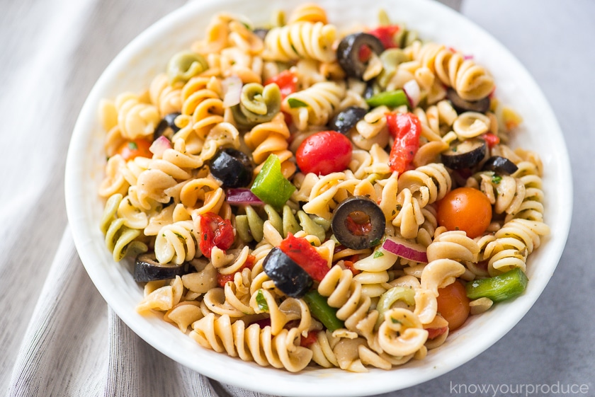 vegan pasta salad with fresh vegetables and olives in a white bowl with beige napkin to the left