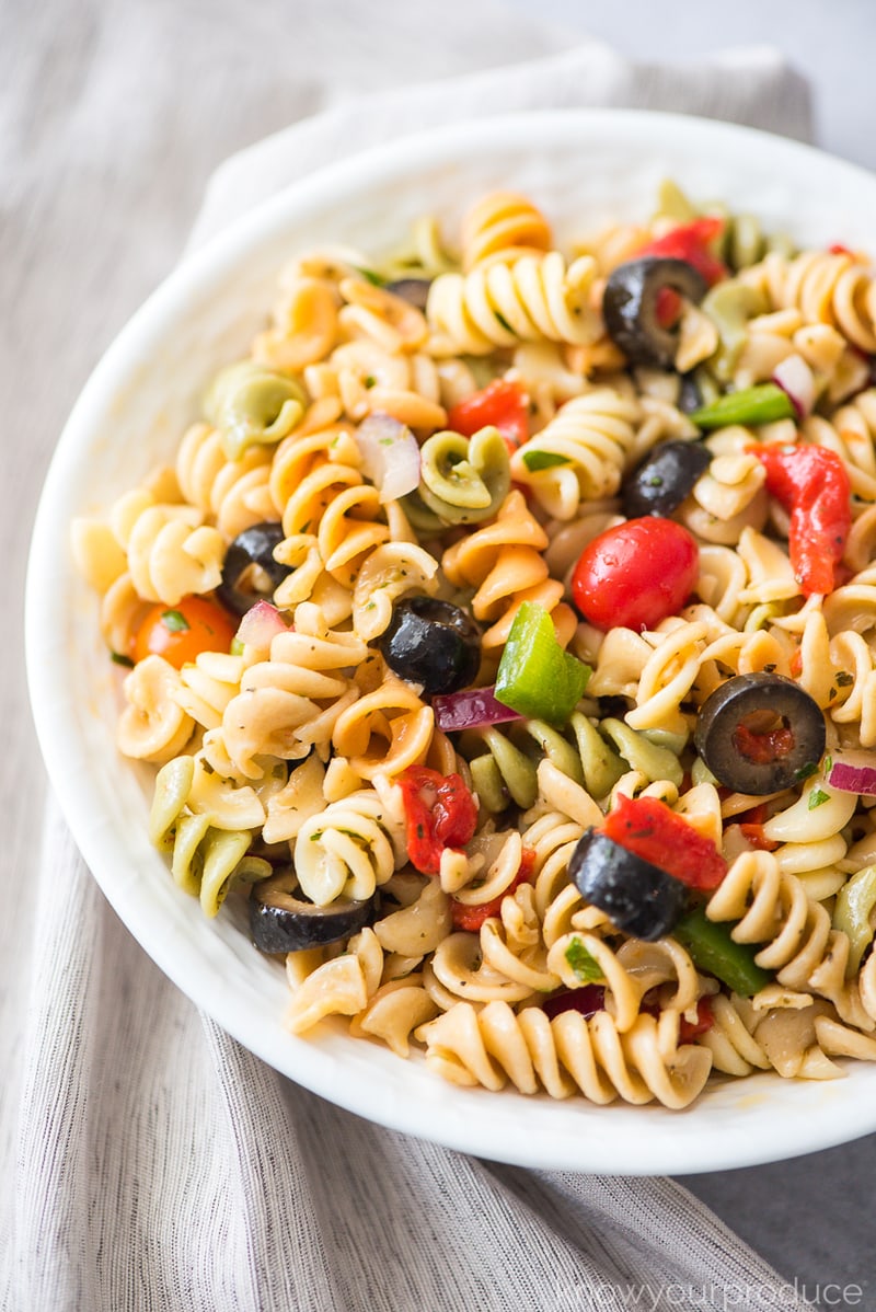 italian pasta salad with fresh vegetables and olives in a white bowl with beige napkin to the left