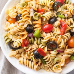 vegan pasta salad with fresh vegetables and olives in a white bowl with beige napkin to the left