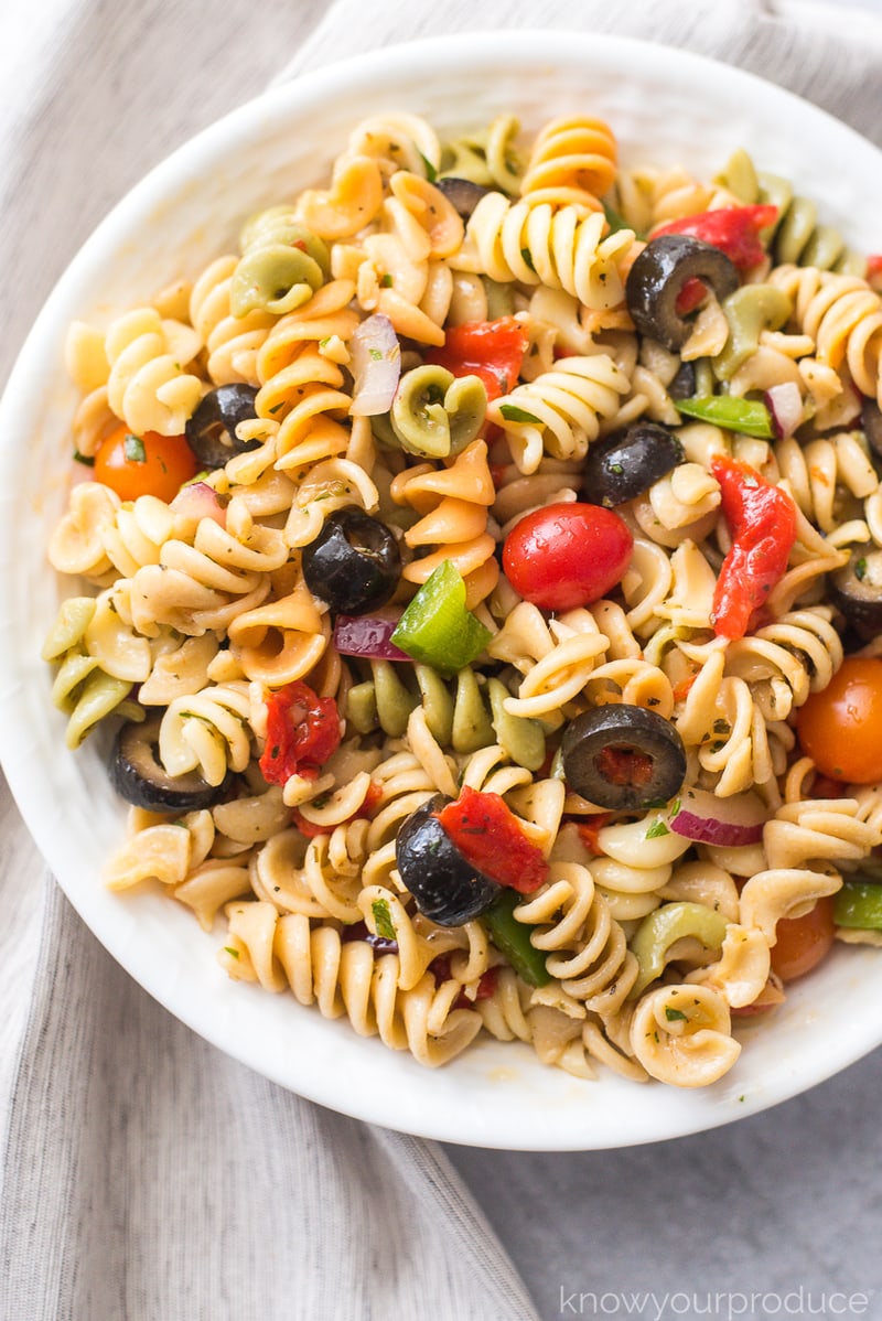 vegan pasta salad with fresh vegetables and olives in a white bowl with beige napkin to the left