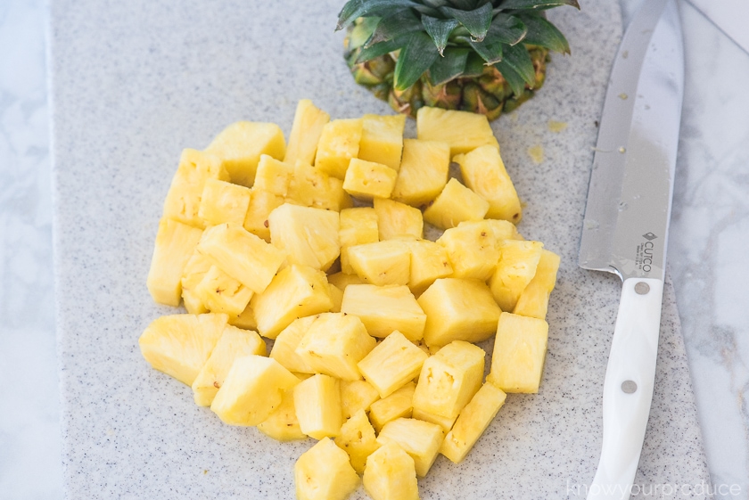 fresh cut pineapple chunks on a cutting board with a knife