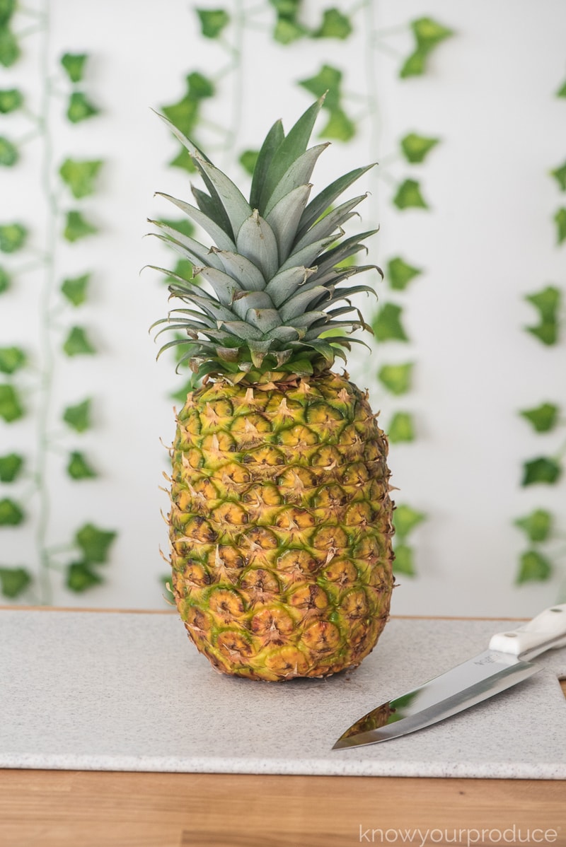 whole pineapple on a cutting board with knife and greenery in the background