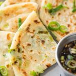 chinese scallion pancakes cut on a plate with scallion garnish and sauce to the side