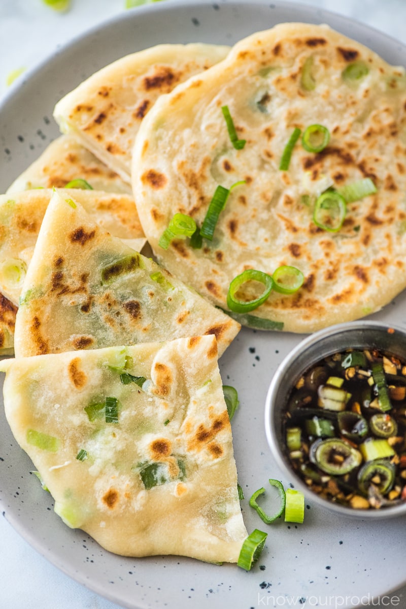 chinese scallion pancakes cut on a plate with dipping sauce on the side