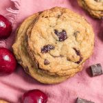 cherry chocolate chip cookies on a pink napkin with chocolate and cherries scattered