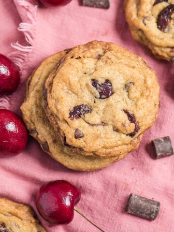 cherry chocolate chip cookies on a pink napkin with chocolate and cherries scattered