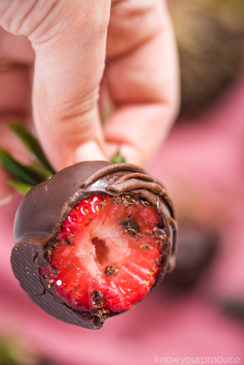 chocolate covered strawberry behind held in a hand with a bite taken out