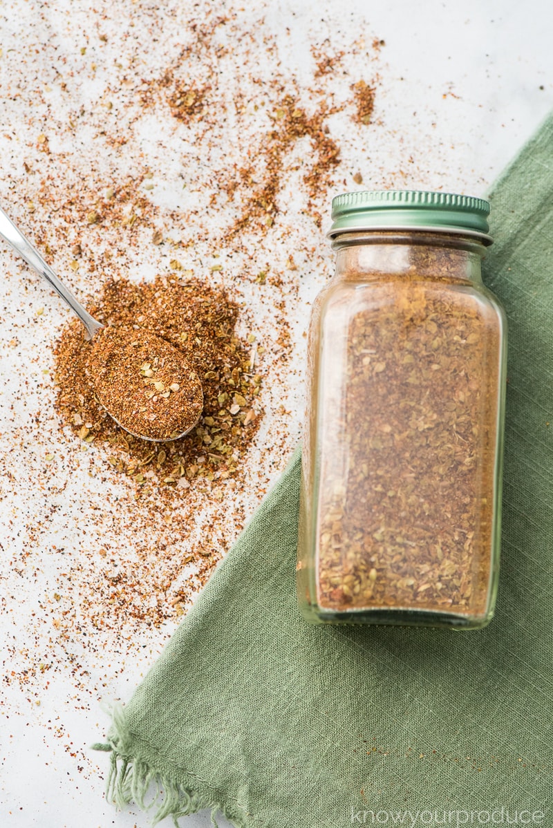 homemade taco seasoning mix in a glass spice jar with seasoning on a spoon with green napkin
