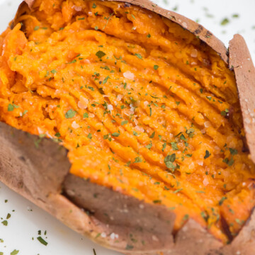 fork mashed air fryer sweet potato seasoned with kosher salt and parsley on a white plate