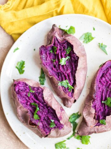 open and fork mashed baked purple sweet potato on a beige speckled plate with fresh parsley on a yellow napkin
