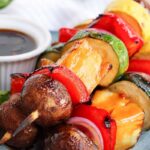 vegetable kabobs on a plate with teriyaki glaze in a white dipping container