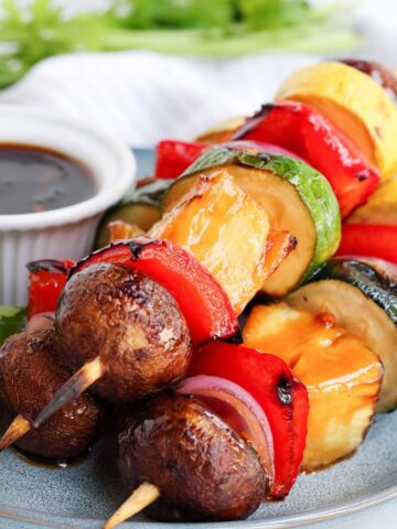 vegetable kabobs on a plate with teriyaki glaze in a white dipping container