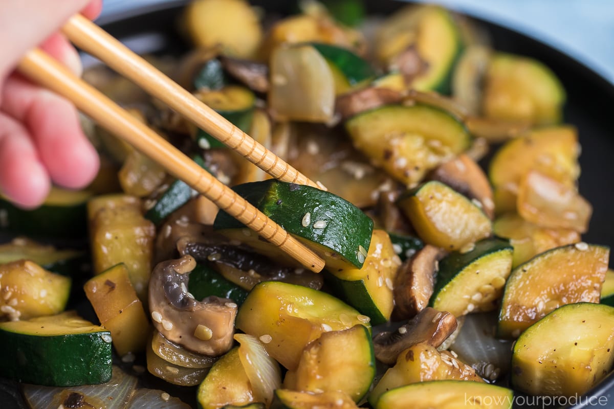 chopsticks grabbing zucchini on plate of hibachi veggies