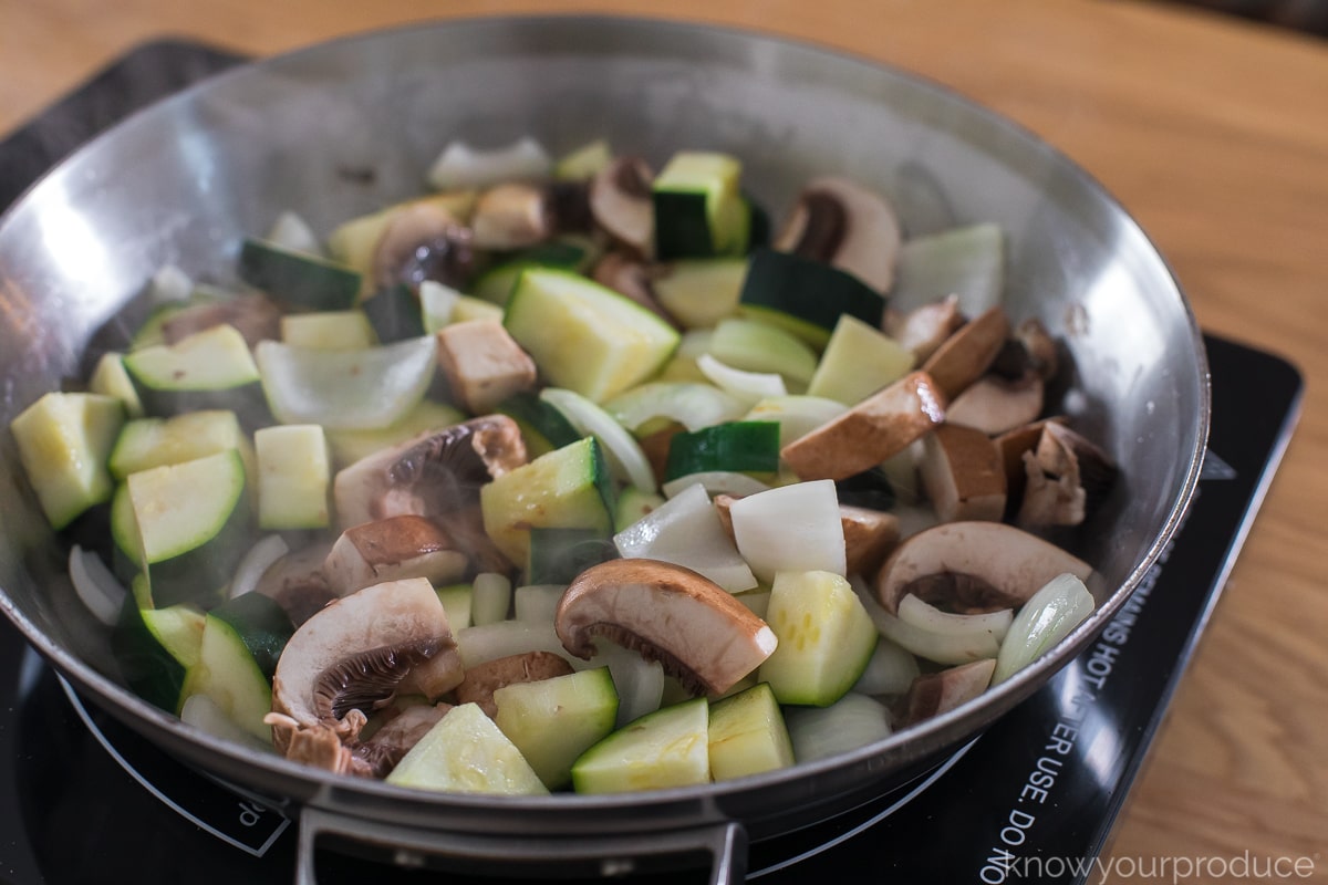 mushrooms, zucchini, and onions cooking in stainless steel skillet