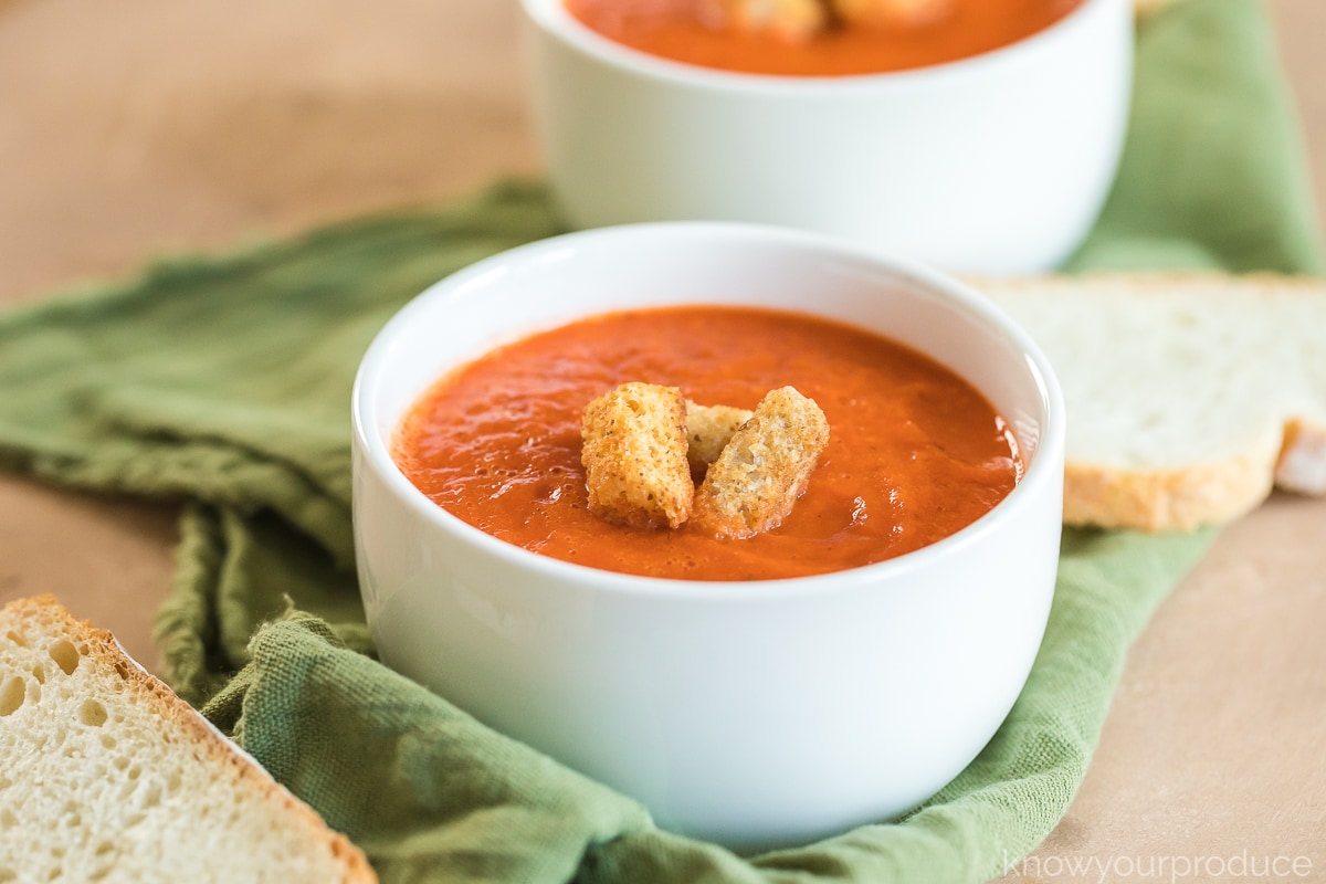 Roasted Red Pepper and Tomato Soup in a white small bowl with croutons inside on a green napkin