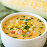 vegan corn chowder in a small white bowl on a green napkin and an ear of corn in background