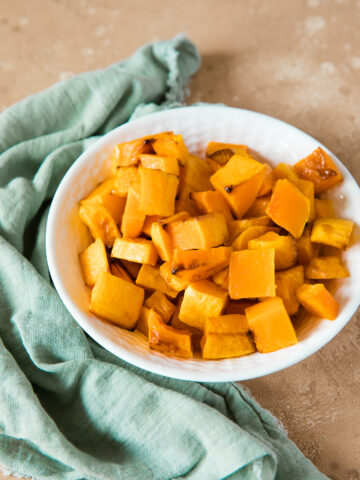 air fryer butternut squash in a white bowl with teal napkin on the side