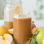 homemade apple cider in a glass cup with apples around it and half filled mason jar behind it