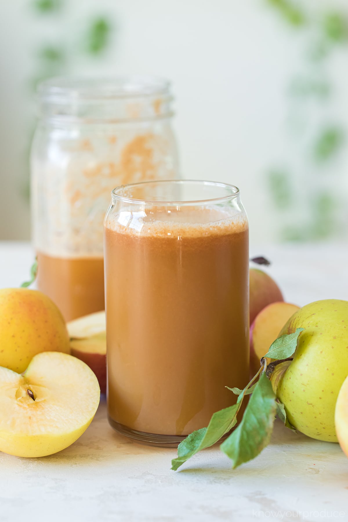 homemade apple cider in a glass cup with apples around it and half filled mason jar behind it