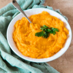 mashed butternut squash with parsley garnish in a bowl with a spoon with a teal napkin on the side