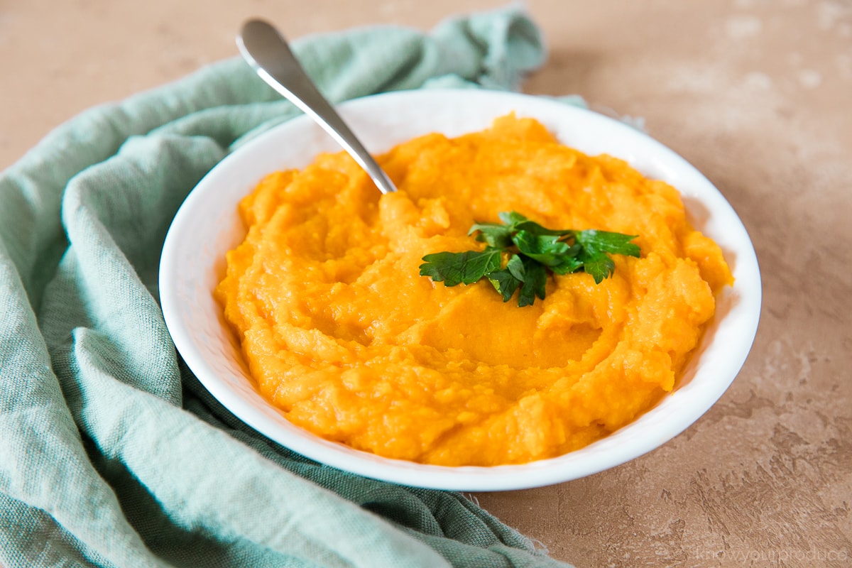parsley garnished mashed butternut squash in a bowl with a spoon with a teal napkin on the side