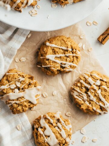 pumpkin oatmeal cookies on unbleached parchment paper styled next to a plate with more cookies
