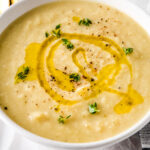 cauliflower leek soup in a white bowl with olive oil drizzle and thyme garnish