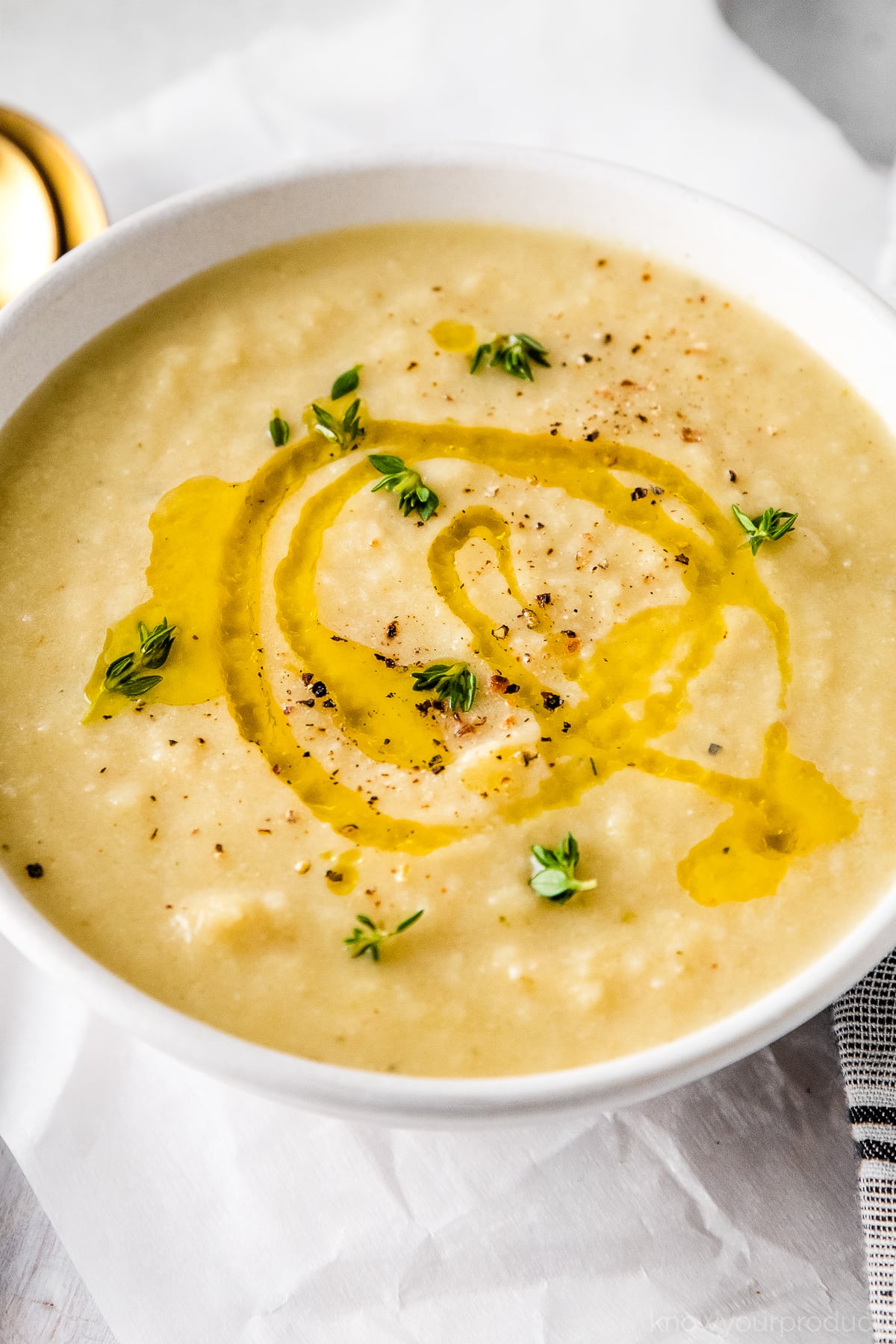 cauliflower leek soup in a white bowl with olive oil drizzle and thyme garnish