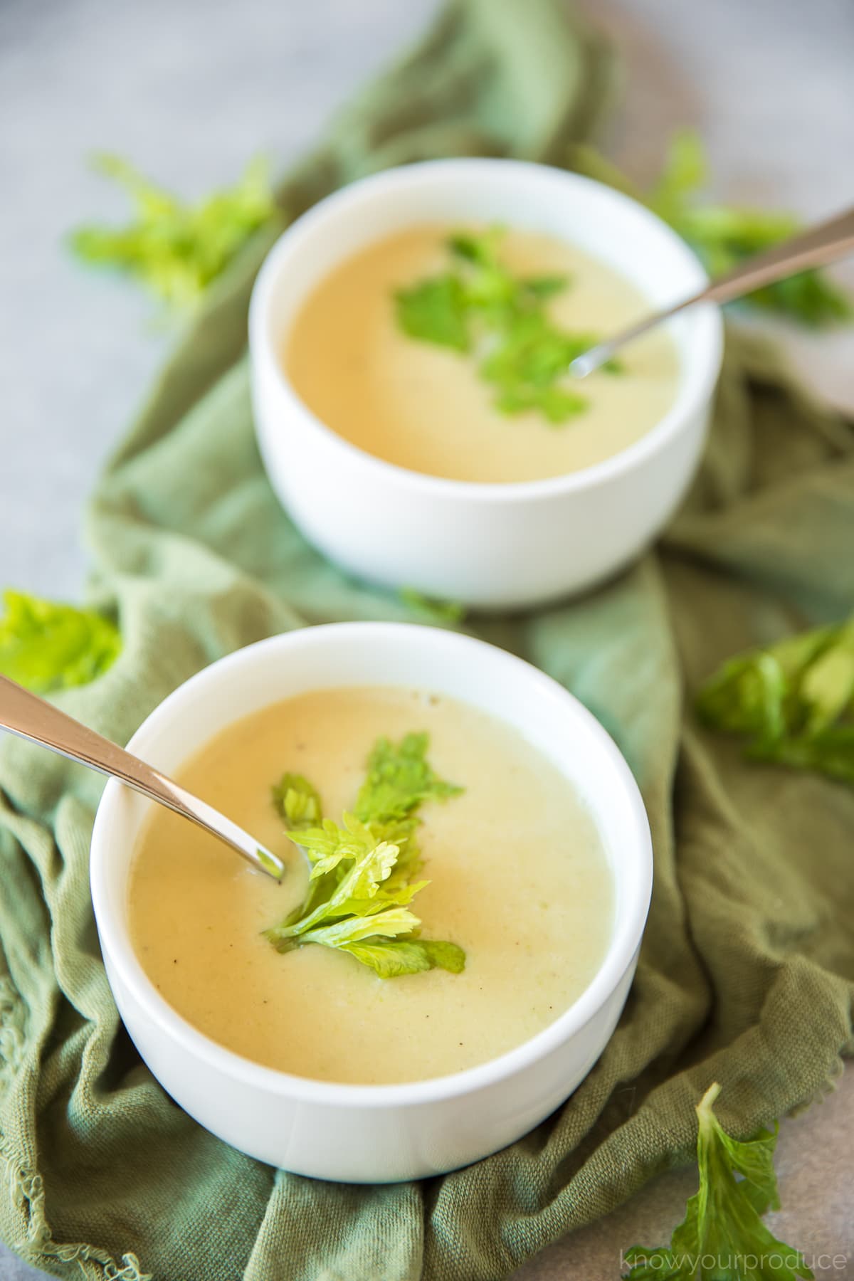 two bowls of cream of celery soup in white bowls on a green napkin