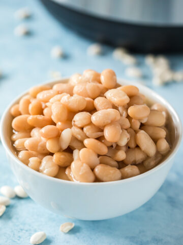 cooked instant pot white beans in a white bowl with instant pot in background