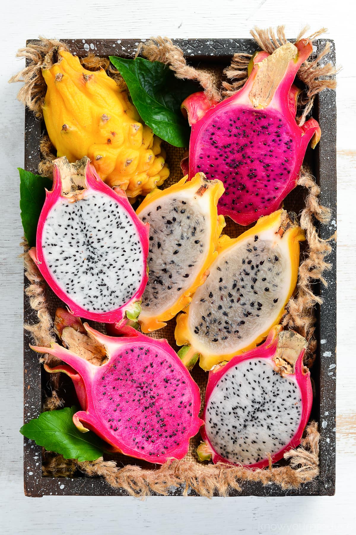 all 3 types of dragon fruit cut in half lengthwise showing inside in a wooden box with fabric 