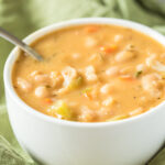 creamy white bean soup in a white bowl with spoon on a green napkin
