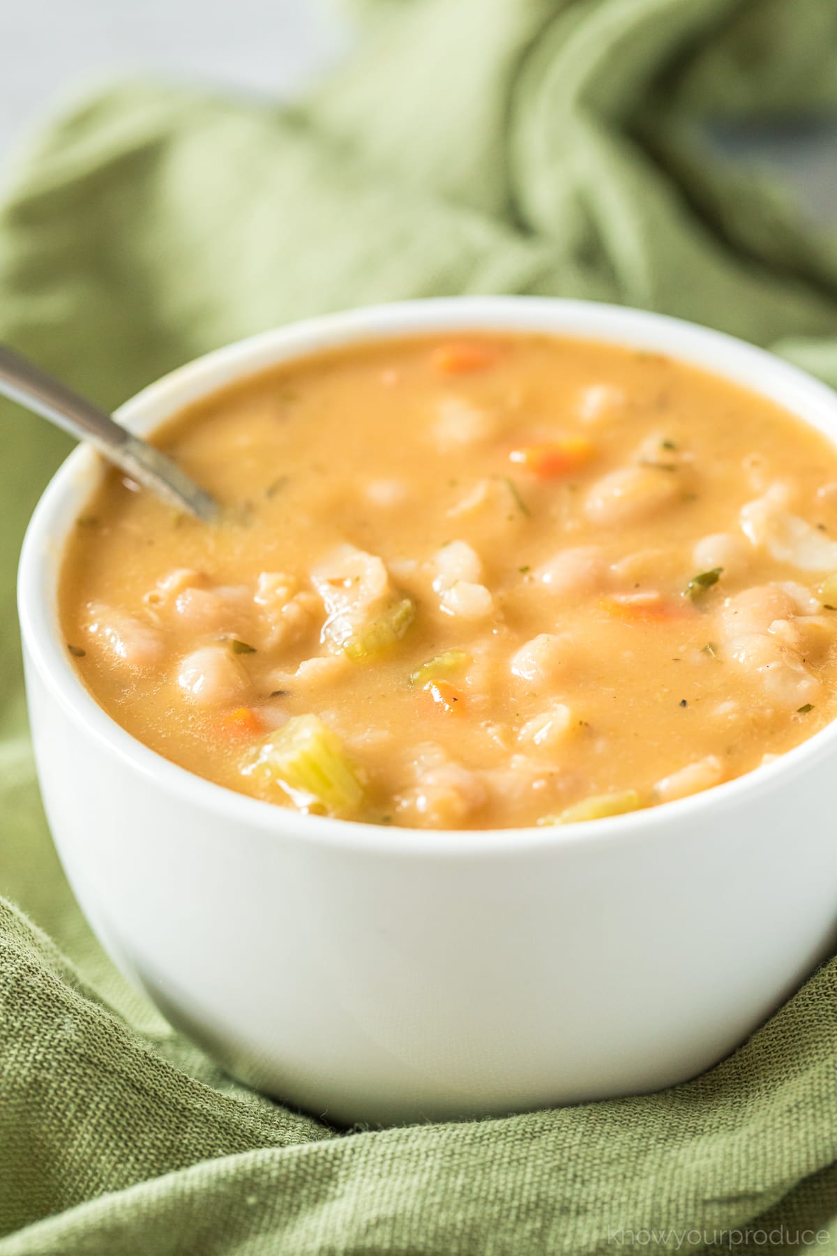 creamy white bean soup in a white bowl with spoon on a green napkin