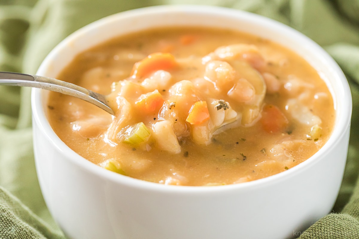 creamy white bean soup in a white bowl with spoon holding up a bite full on a green napkin