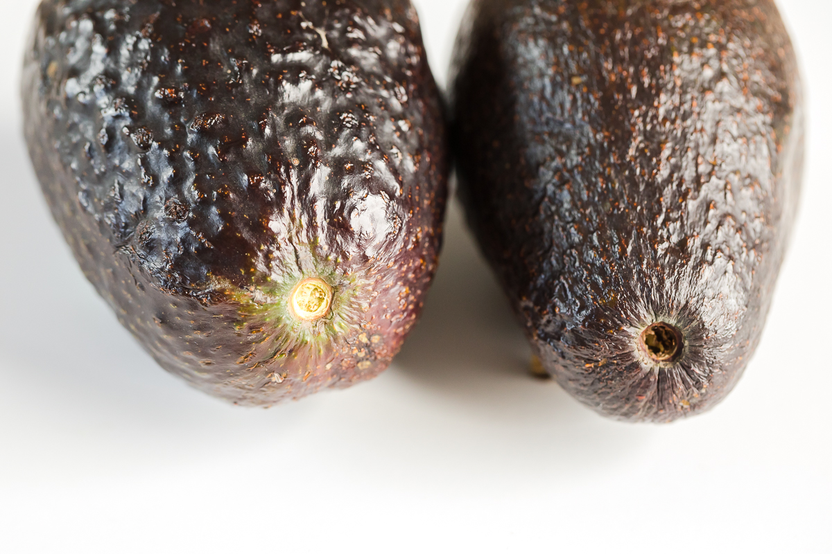 how to pick an avocado with stem showing left with stem freshly remove and green inside and right avocado brown inside missing stem from purchase.