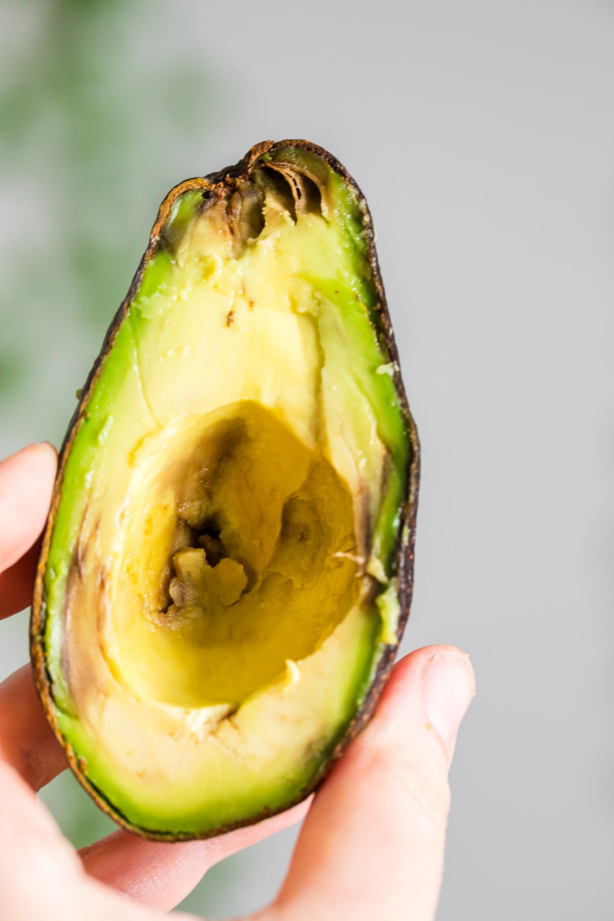 hand holding an overripe avocado half without seed.