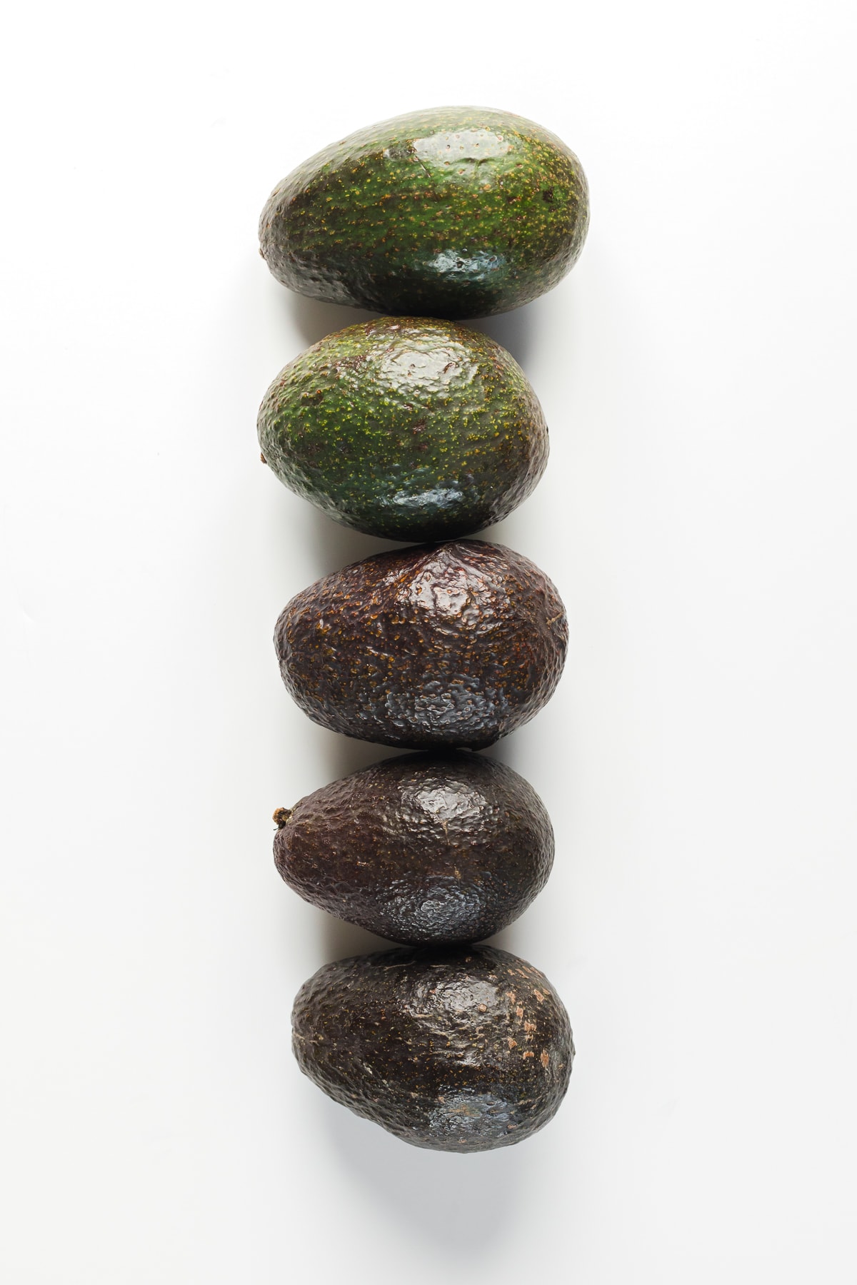 5 avocados showing going green on the top and then getting darker and more ripe to black avocados on the bottom.