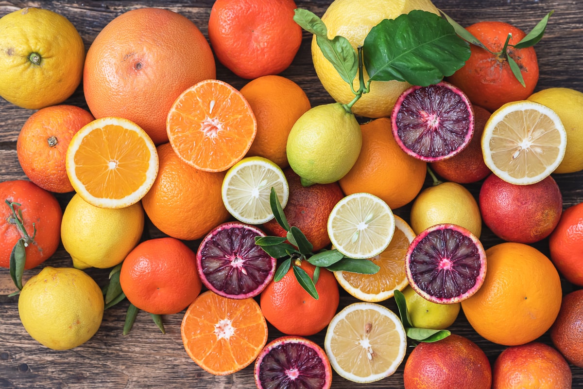 various citrus fruits on a wooden table with some whole and some sliced in half to show inside.