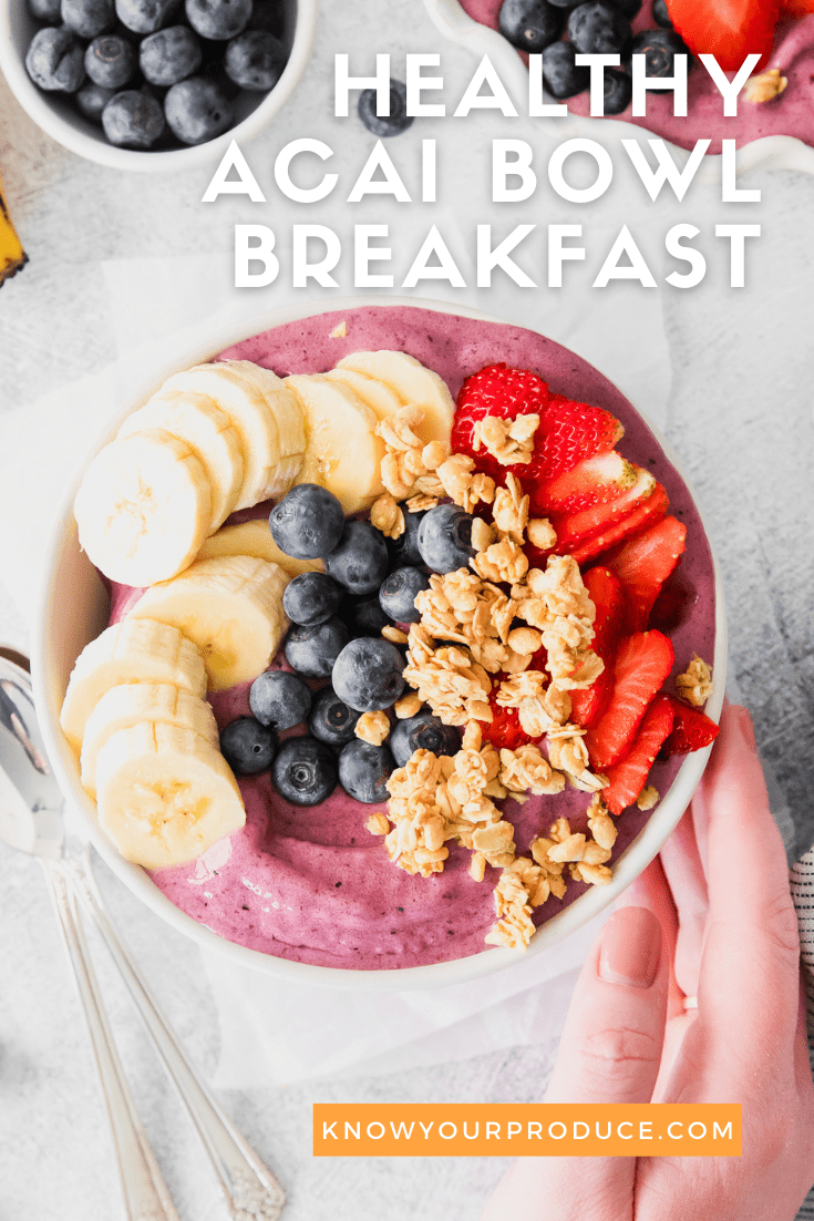 hand holding a white bowl that is filled with a thick acai smoothie topped with sliced banana, granola, blueberries, and sliced strawberries with text on image for pinterest.