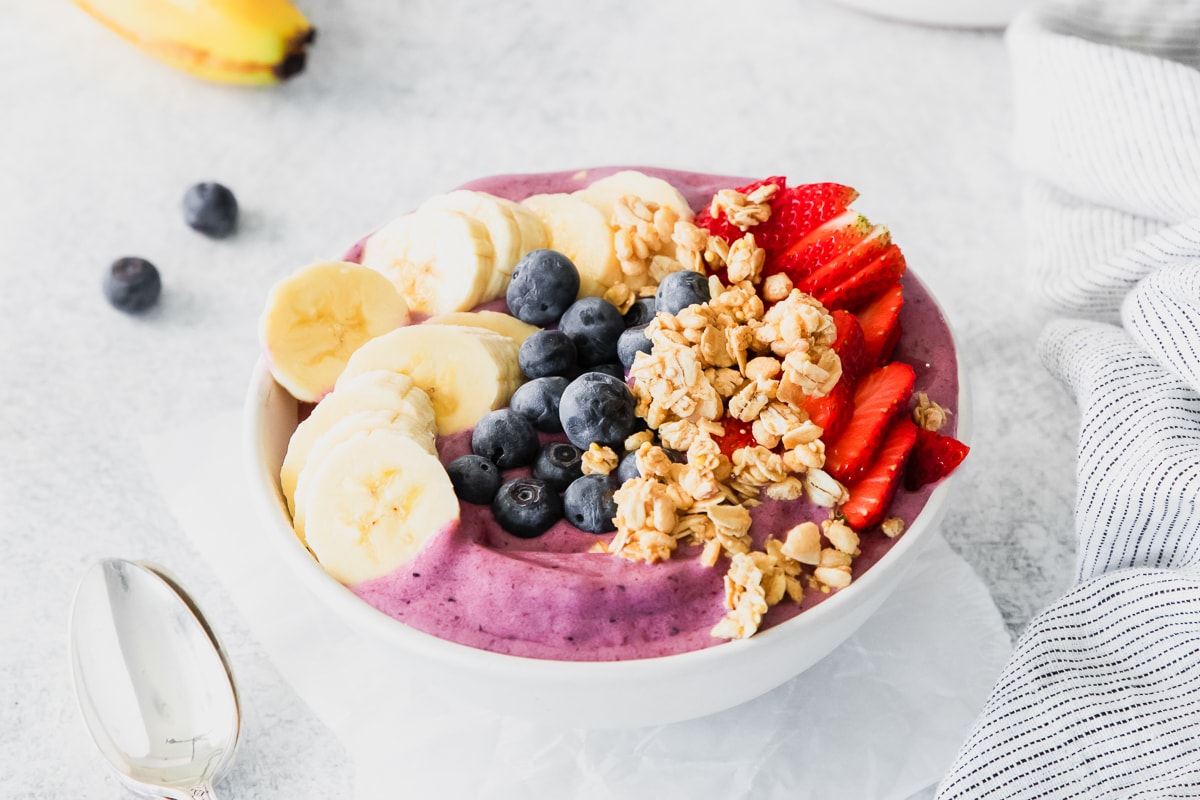 acai bowl topped fresh fruit, granola, and a spoon to the left.