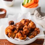 air fryer cauliflower wings in a white low bowl lined with parchment paper.